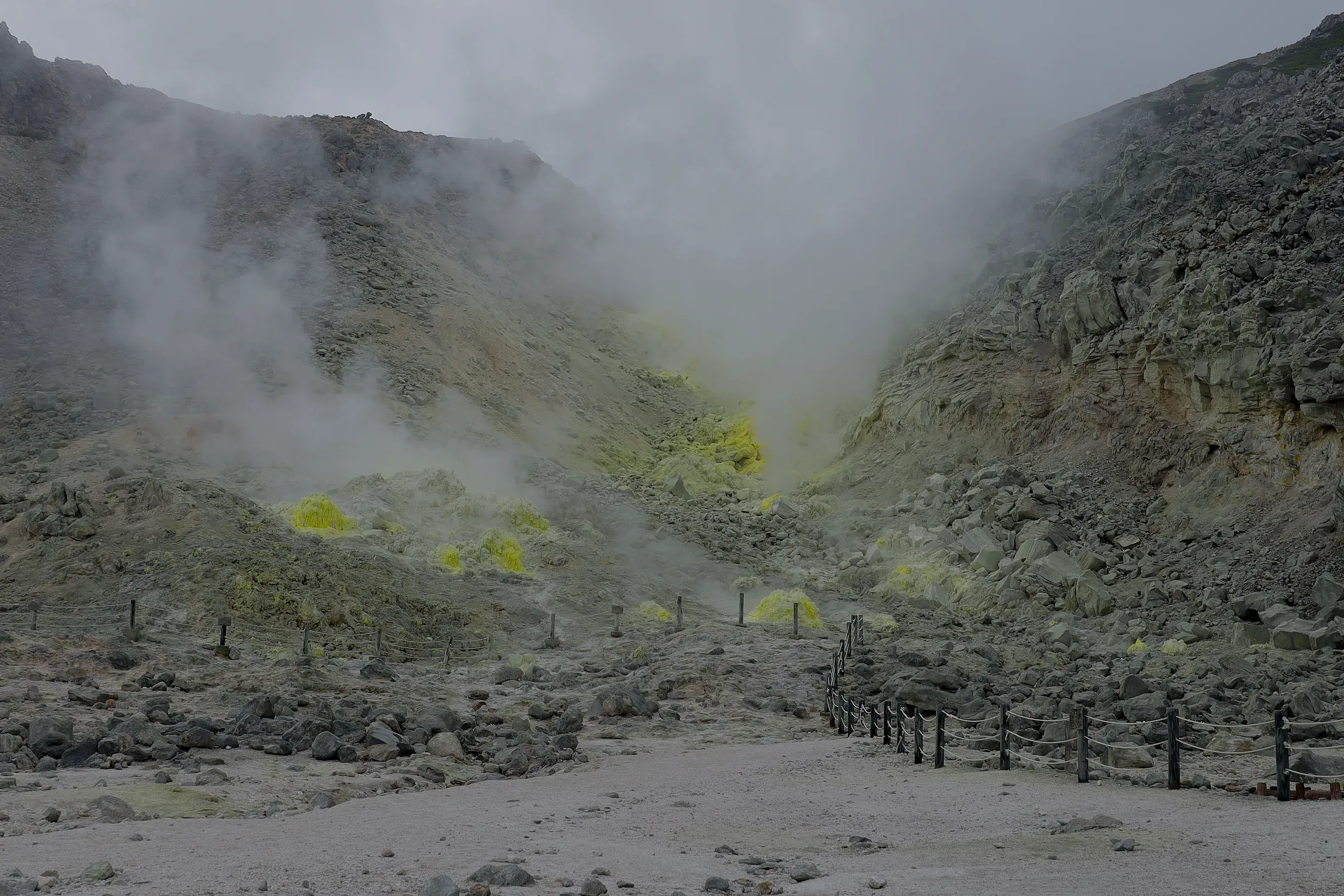 Steam rising from the yellow sulfur fumaroles of Mt. Iō, a roped path leading into the valley, Hokkaido